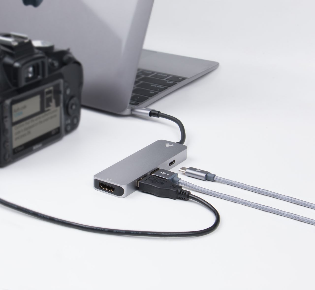 Close-up of a laptop, camera, and connected cables on a desk, depicting modern technology.